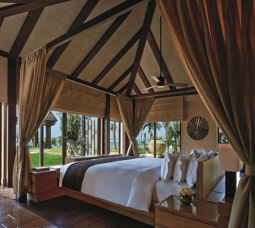 Elegantes Schlafzimmer mit freiliegenden Holzbalken und Blick auf das Meer durch große Fenster.