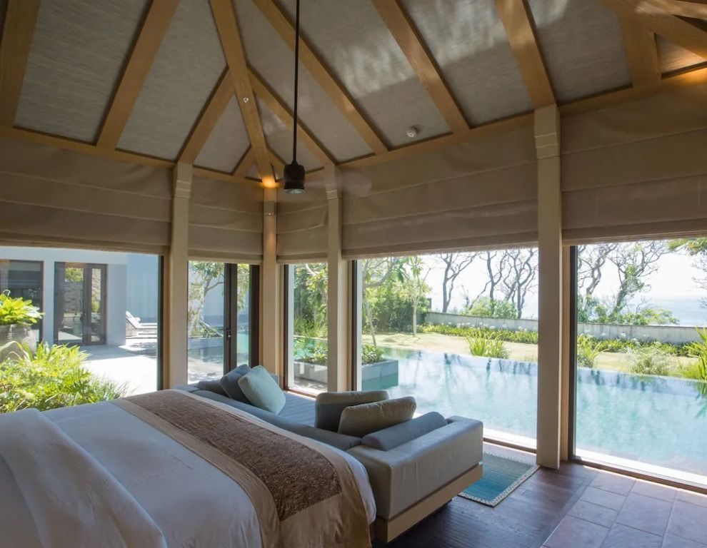 Schlafzimmer mit Ausblick auf privaten Pool durch große Fenster.