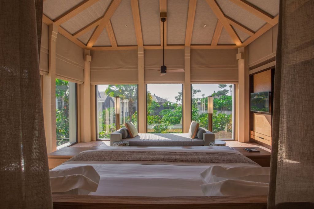Luxuriöse Villa mit großem Bett und bodentiefen Fenstern mit Blick ins Grüne.