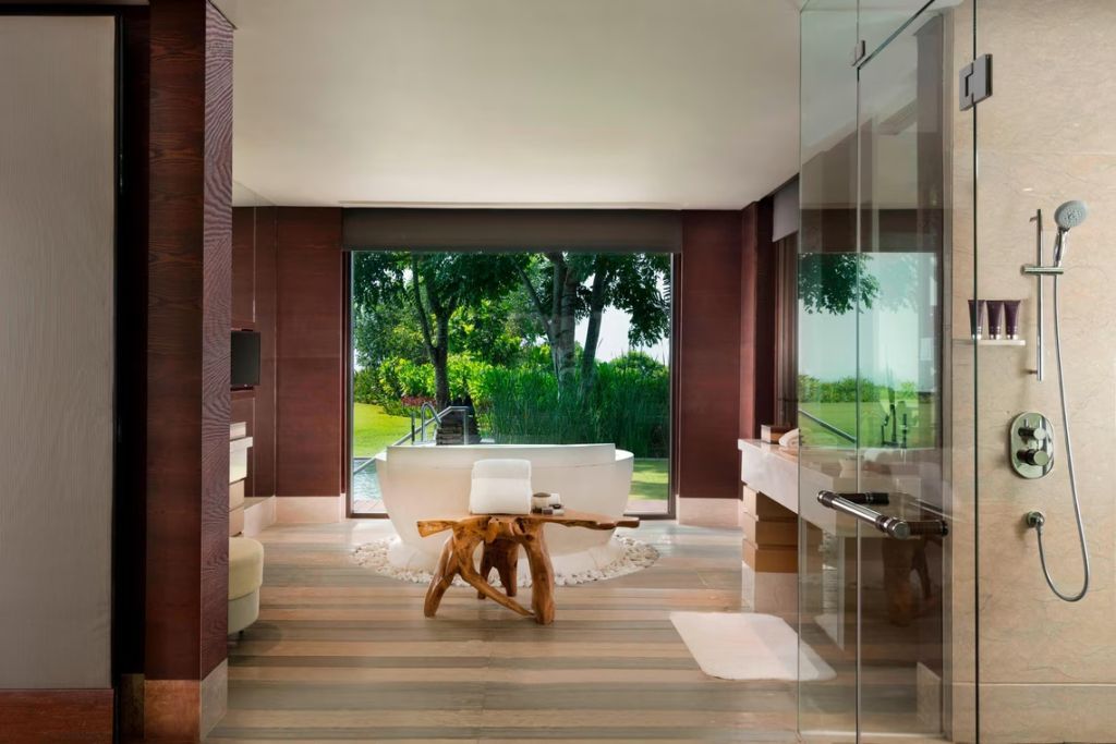 Luxuriöses Badezimmer mit freistehender Badewanne und Blick auf grünen Garten.