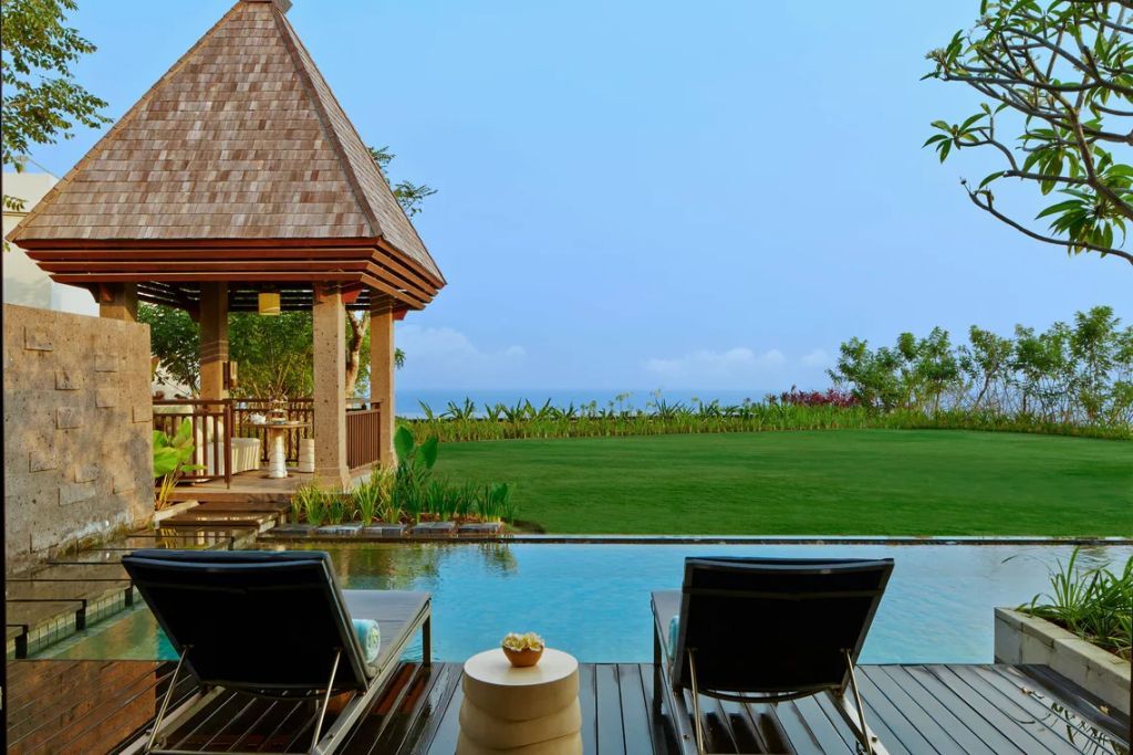 Privater Infinity-Pool mit Garten und Blick auf das Meer, zwei Liegestühle davor.