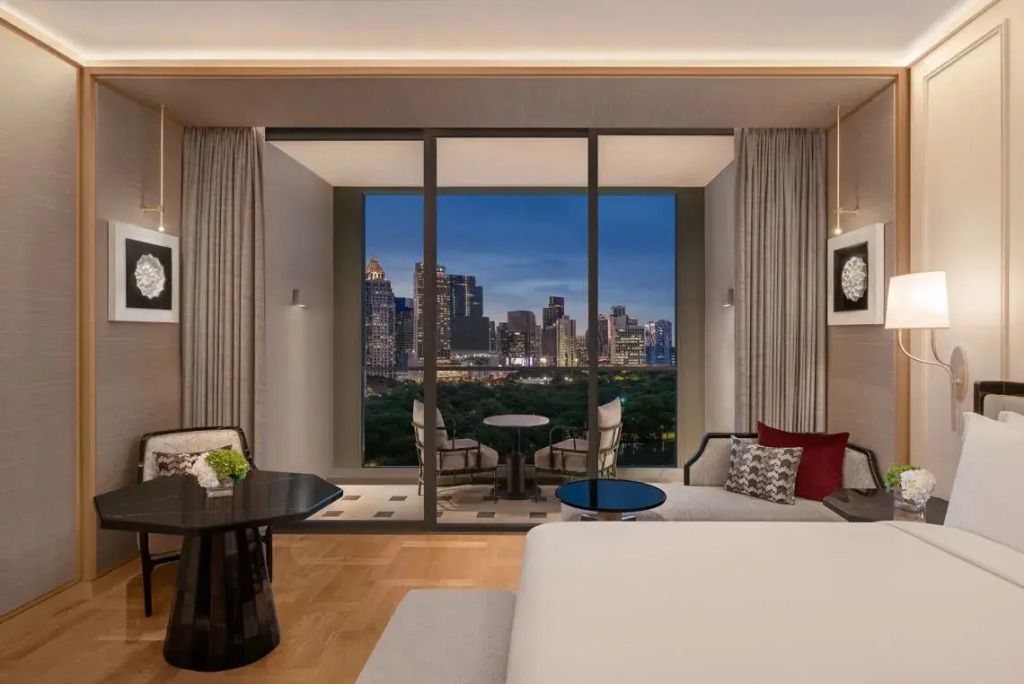 Elegantes Zimmer mit großem Bett, Balkon und Blick auf die Skyline von Bangkok bei Nacht.