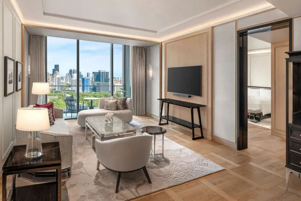 Moderner Wohnbereich der Suite mit Balkon und Blick auf Lumpini Park und Skyline.