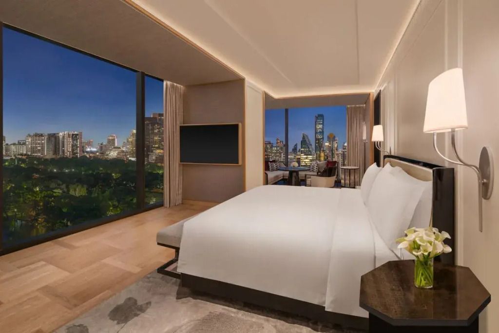 Gemütliches Schlafzimmer mit Nachtansicht auf die erleuchtete Skyline von Bangkok.