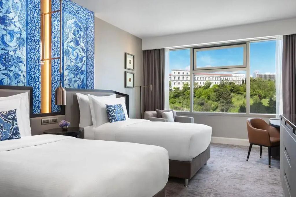 Zimmer mit zwei Einzelbetten und großem Fenster mit Blick auf die Stadt