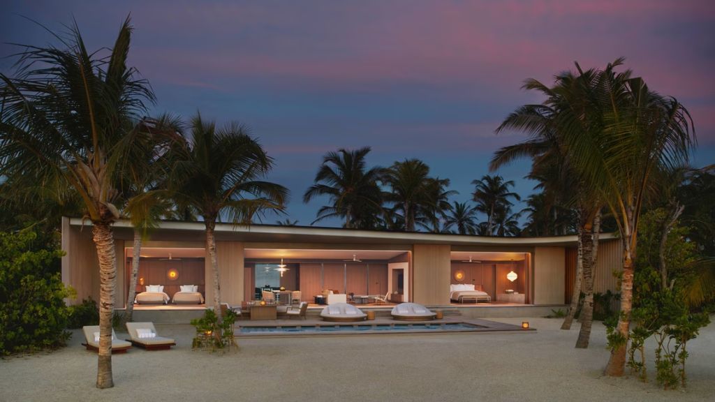 Beach Pool Villa bei Sonnenuntergang mit offenem Wohnraum, Pool und Palmen im Hintergrund.