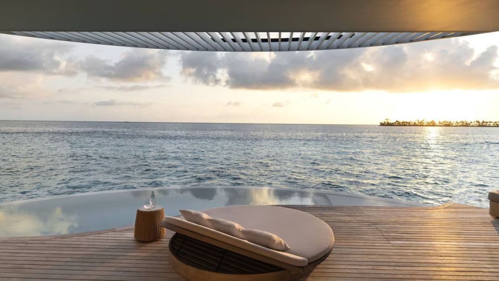Sonnenuntergang über dem Meer gesehen von einer Holzterrasse mit Liegen