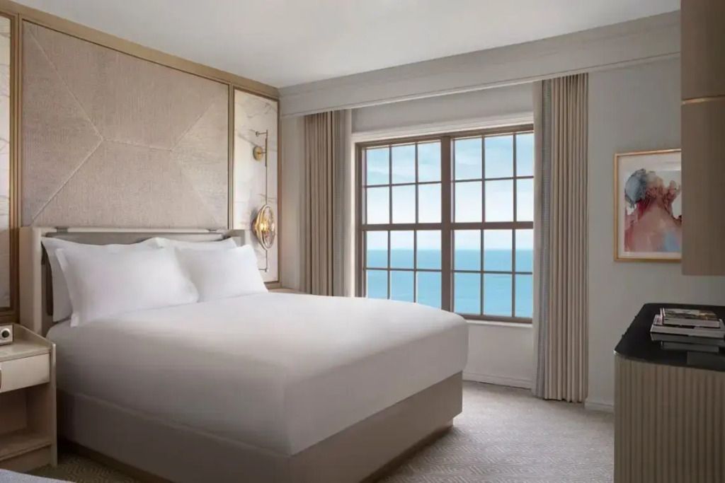 Helles Schlafzimmer mit Doppelbett und Meerblick aus einem großen Fenster