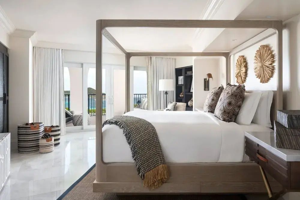Helles Schlafzimmer mit Himmelbett und dekorativen Kissen vor einer Fensterfront
