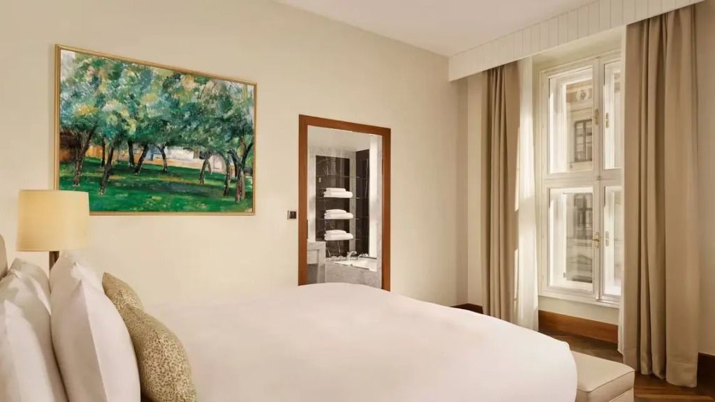Schlafzimmer mit Kunstgemälde und Sicht ins elegante Badezimmer der Albertina Suite.