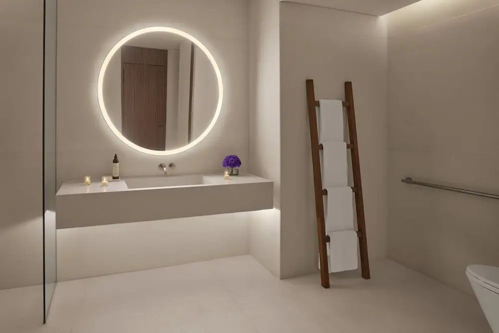 Badezimmer mit rundem beleuchtetem Spiegel, Waschtisch und Handtüchern auf Holzleiter.