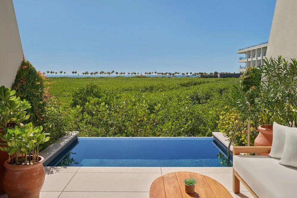 Sonnenterrasse mit kleinem Pool, grünem Ausblick und Blick auf das Meer am Horizont.