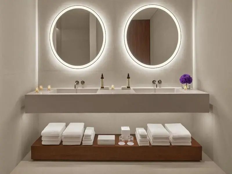 Modern gestaltetes Badezimmer mit Doppelwaschbecken und stilvoll beleuchteten Spiegeln.