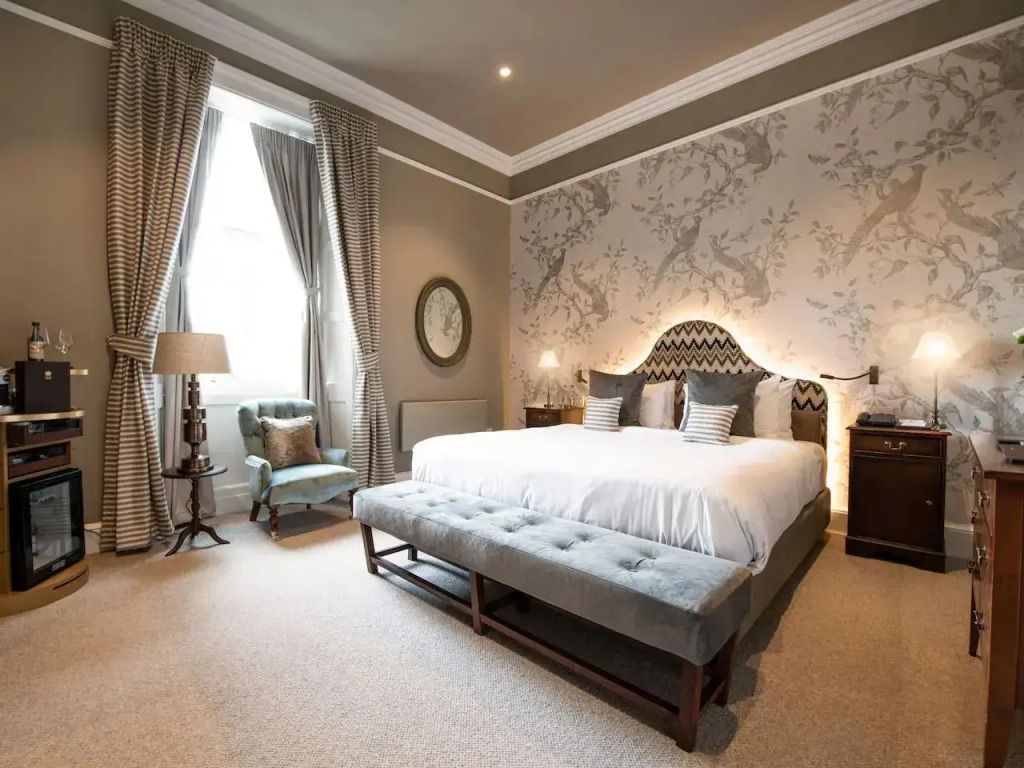 Elegantes Doppelzimmer mit grauem Kopfteil und großen Fenstern.
