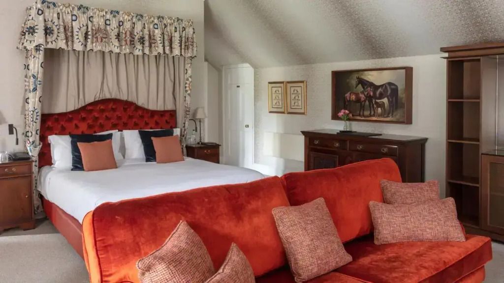 Castle Suite mit rotem Sofa, gemütlichem Bett und Pferdegemälde an der Wand.