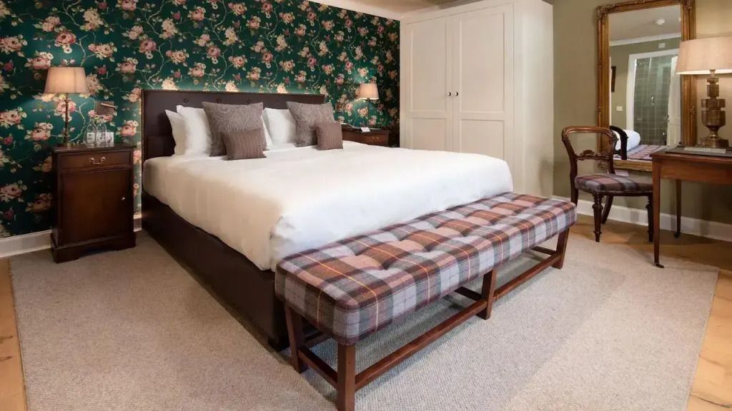 Elegantes Doppelzimmer mit floral gemusterter Tapete, Doppelbett und gepolsterter Bank.
