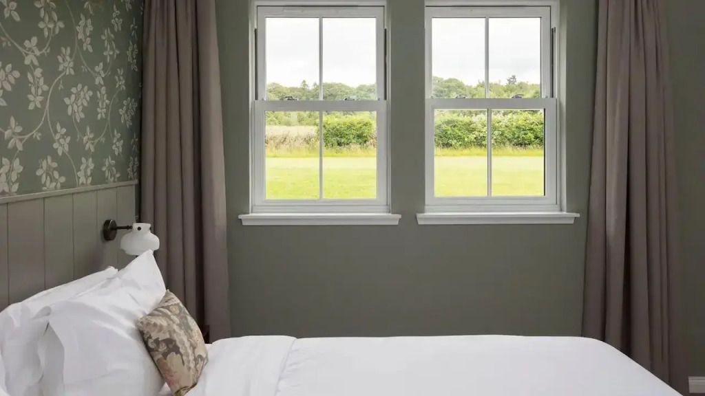 Helles Schlafzimmer mit Aussicht auf grüne Landschaft durch zwei Fenster