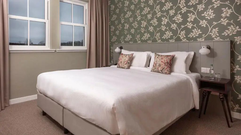 Gemütliches Schlafzimmer mit Doppelbett, florale Tapete und zwei Kissen.