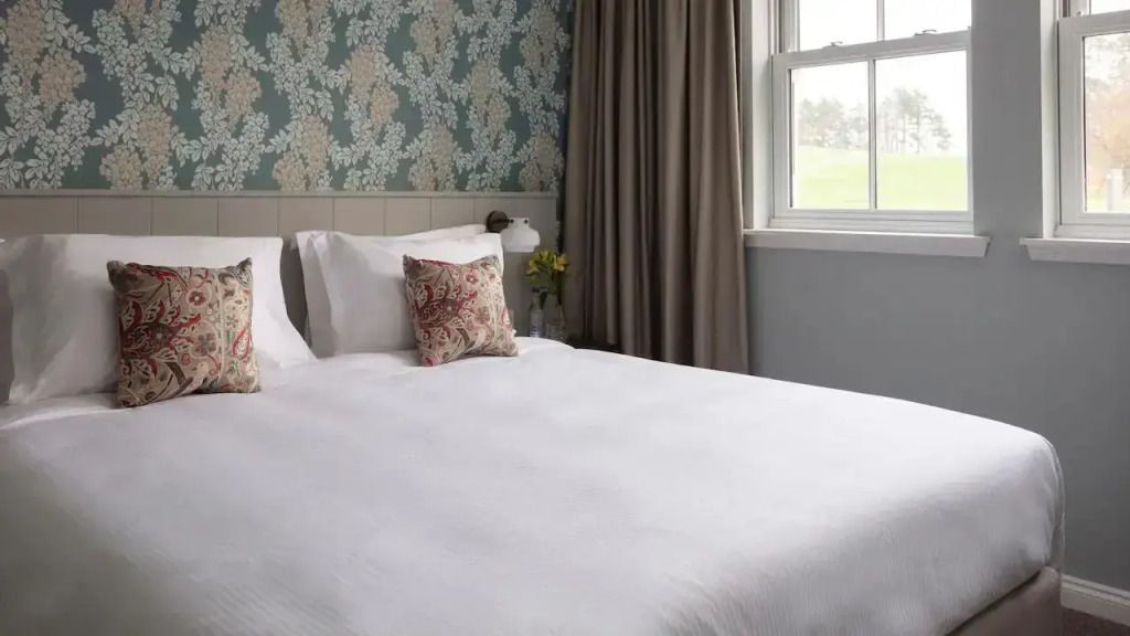 Schlafzimmer mit großem Bett, floraler Tapete und natürlichem Licht.