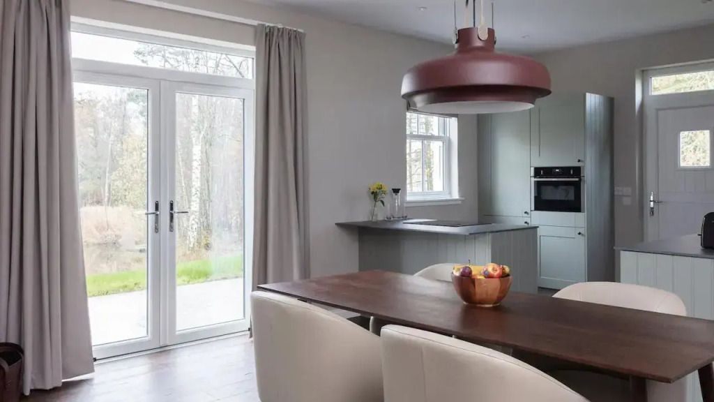 Moderne Küche mit Esstisch, Designlampe und Blick in den Garten.