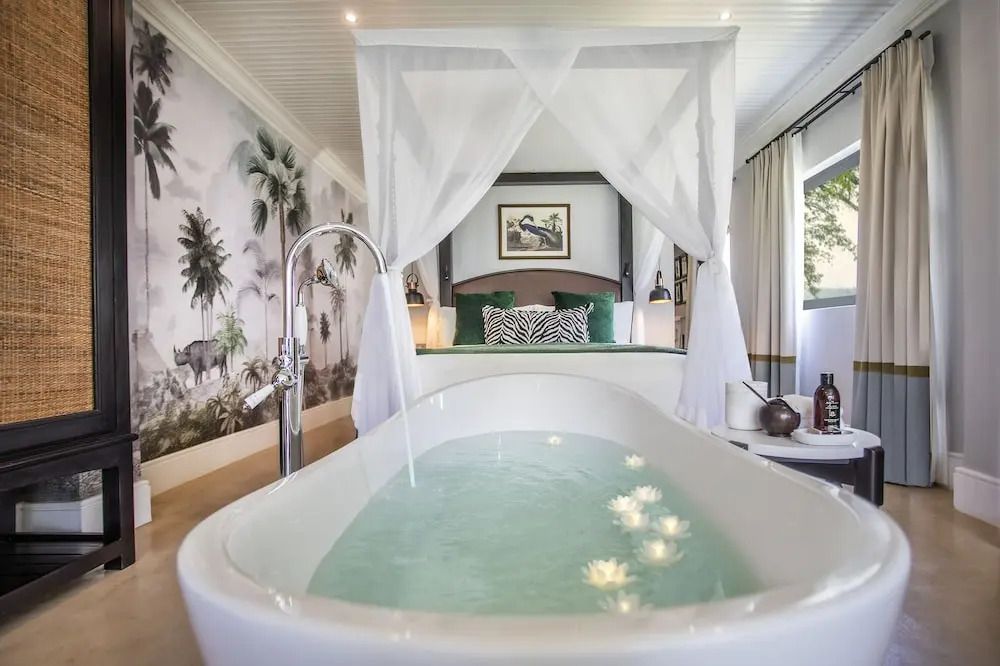 Helles Schlafzimmer mit Himmelbett und gefüllter Badewanne mit Blüten