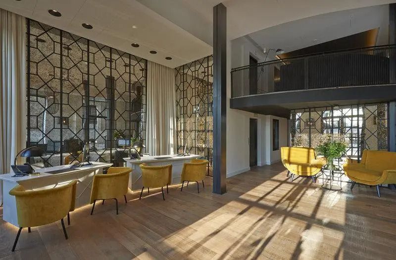 Eleganter Loungebereich mit großen Fenstern und stilvollen gelben Sesseln.