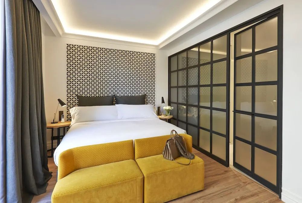 Doppelbett mit stilisierter Kopfleiste und gelbem Sofa im modernen Hotelzimmer