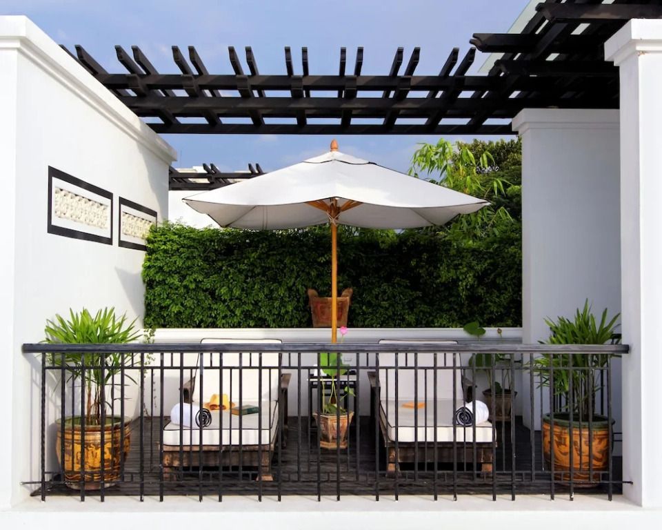 Balkon mit Liegestühlen, Sonnenschirm und grüner Hecke