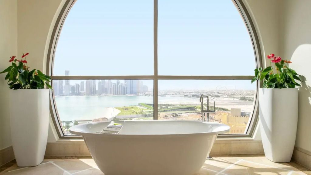 Freistehende Badewanne vor einem großen Fenster mit Blick auf die Skyline von Doha.