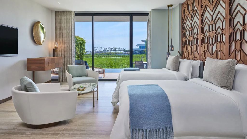 Luxuriöses Hotelzimmer mit zwei Betten und Blick auf grüne Landschaft durch große Fenster.