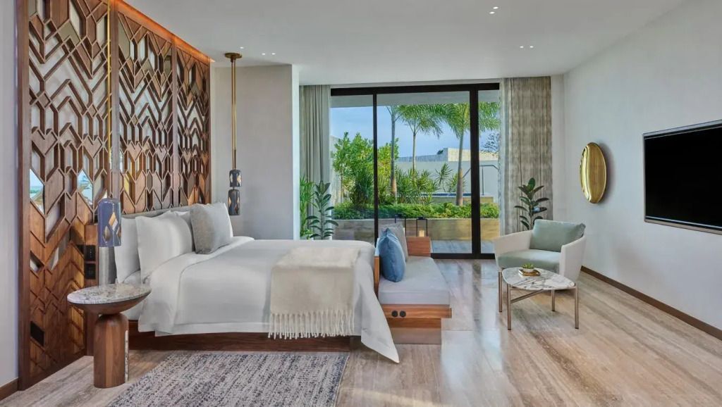 Elegantes Schlafzimmer mit Doppelbett und Blick auf eine private Terrasse mit tropischen Pflanzen.