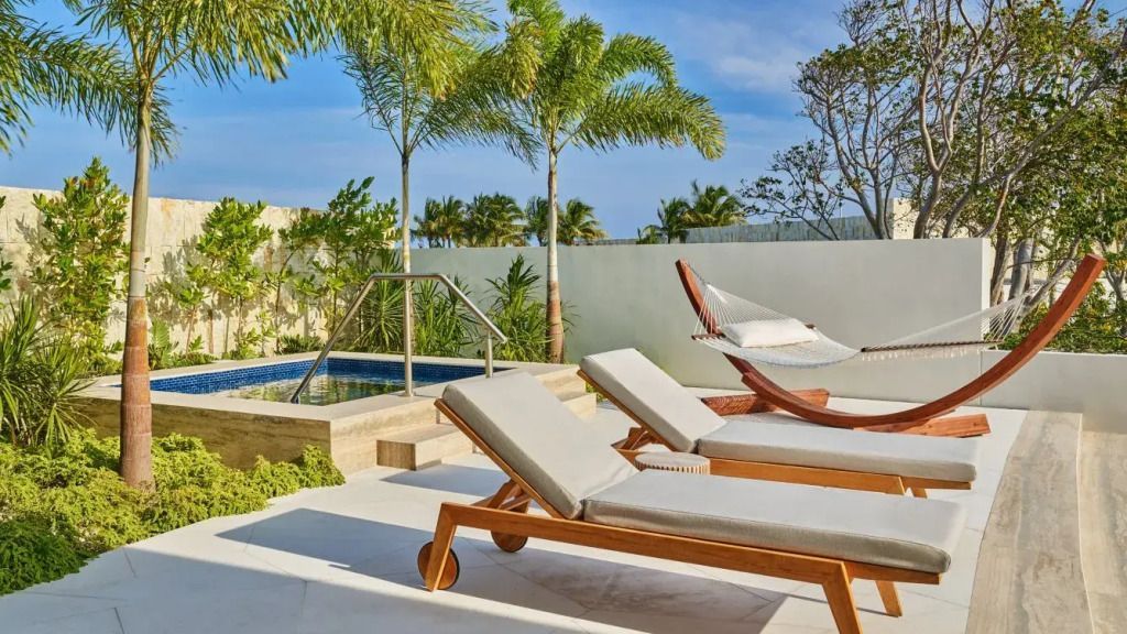 Private Terrasse mit Liegestühlen und Hängematte in tropischer Umgebung.