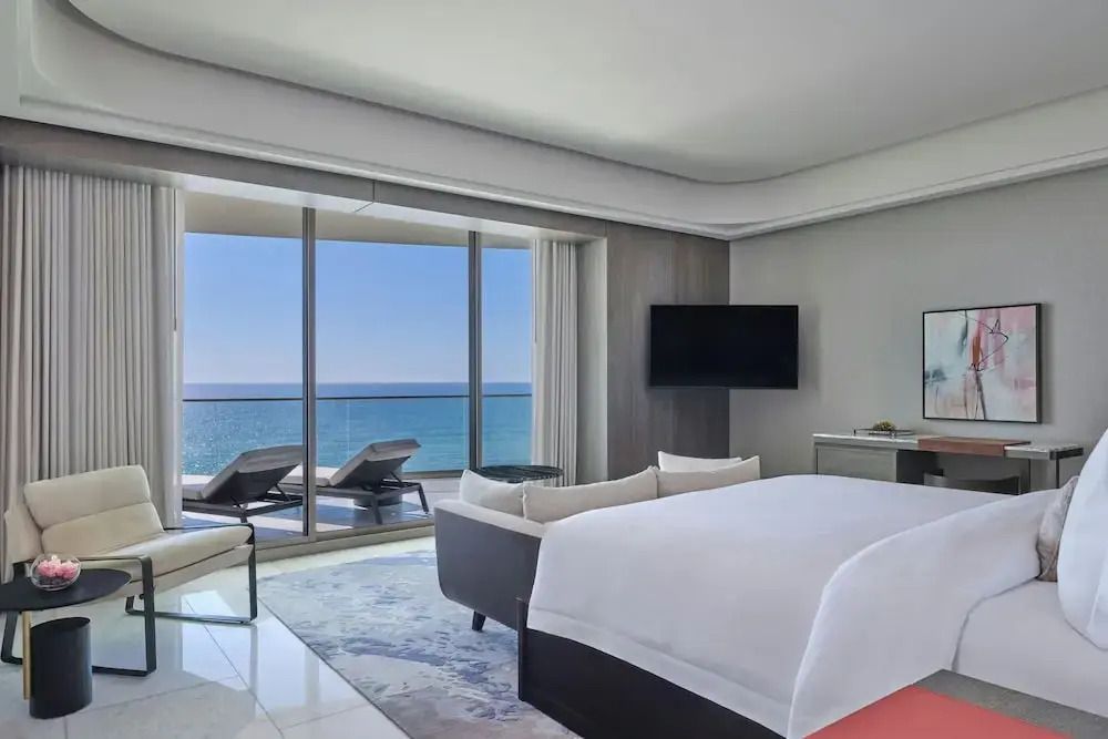 Großes Schlafzimmer mit Meerblick durch bodentiefe Fenster. Helle, moderne Einrichtung.