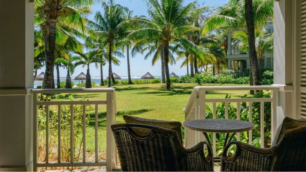 Balkonblick zum palmengesäumten Garten und Meer bei strahlendem Sonnenschein.