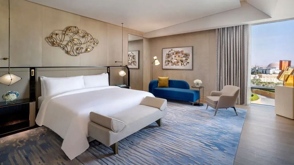 Luxuriöses Schlafzimmer in der St. Regis Suite mit Doppelbett, blauer Couch und Wandkunst