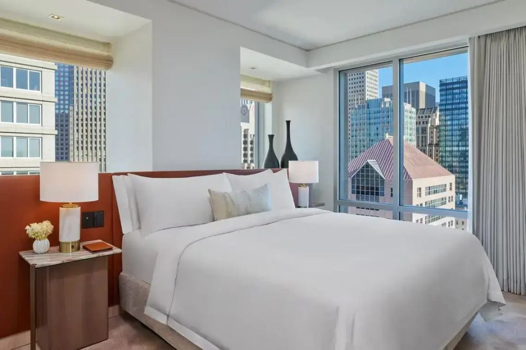 Helles Schlafzimmer mit Doppelbett und Stadtblick durch große Fenster