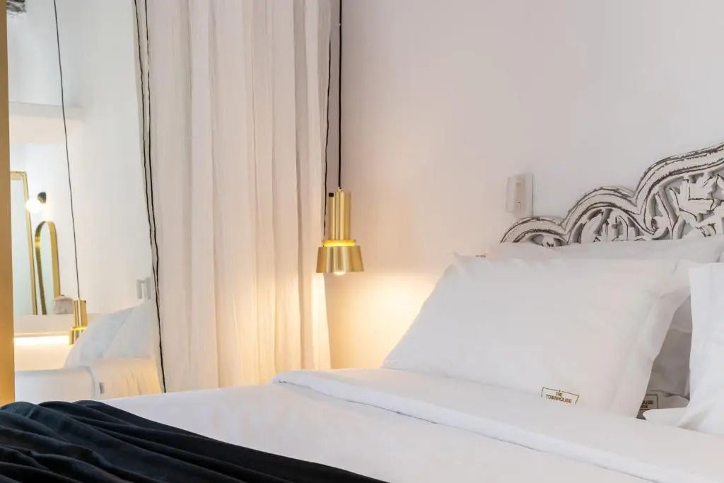 Weißes Bett mit dekorativem Kopfteil und goldener Lampe im Deluxe Zimmer.
