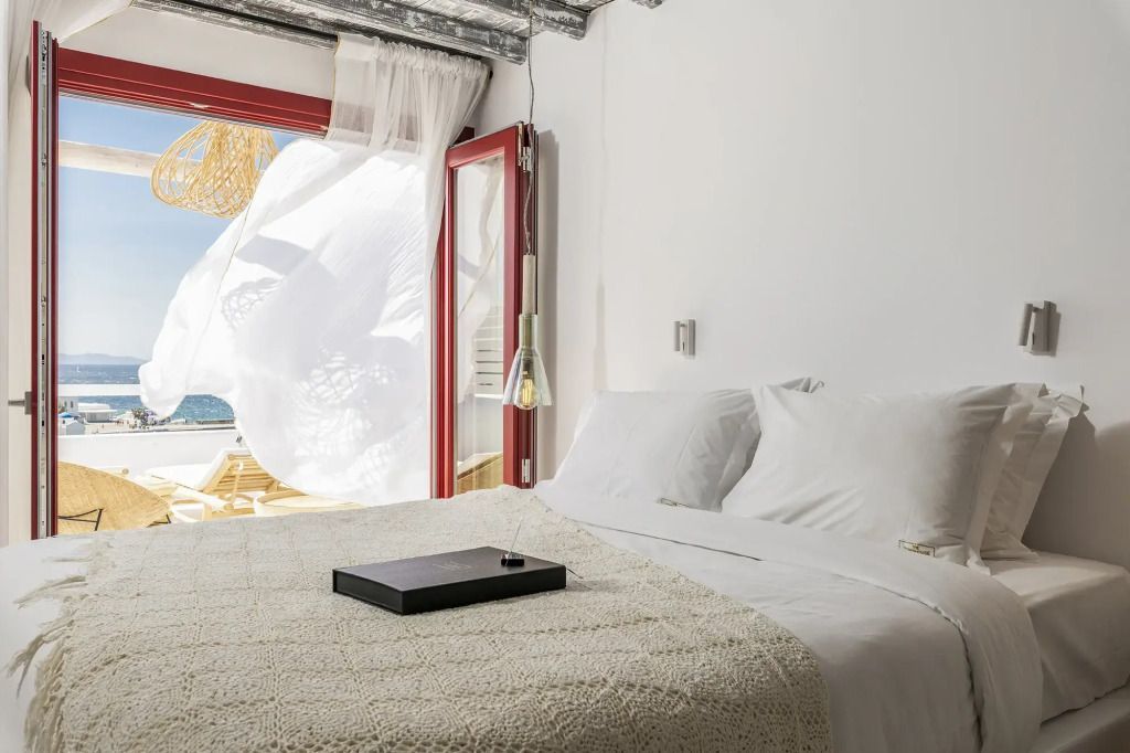 Helles Schlafzimmer mit offenem Fenster und Blick auf das Meer
