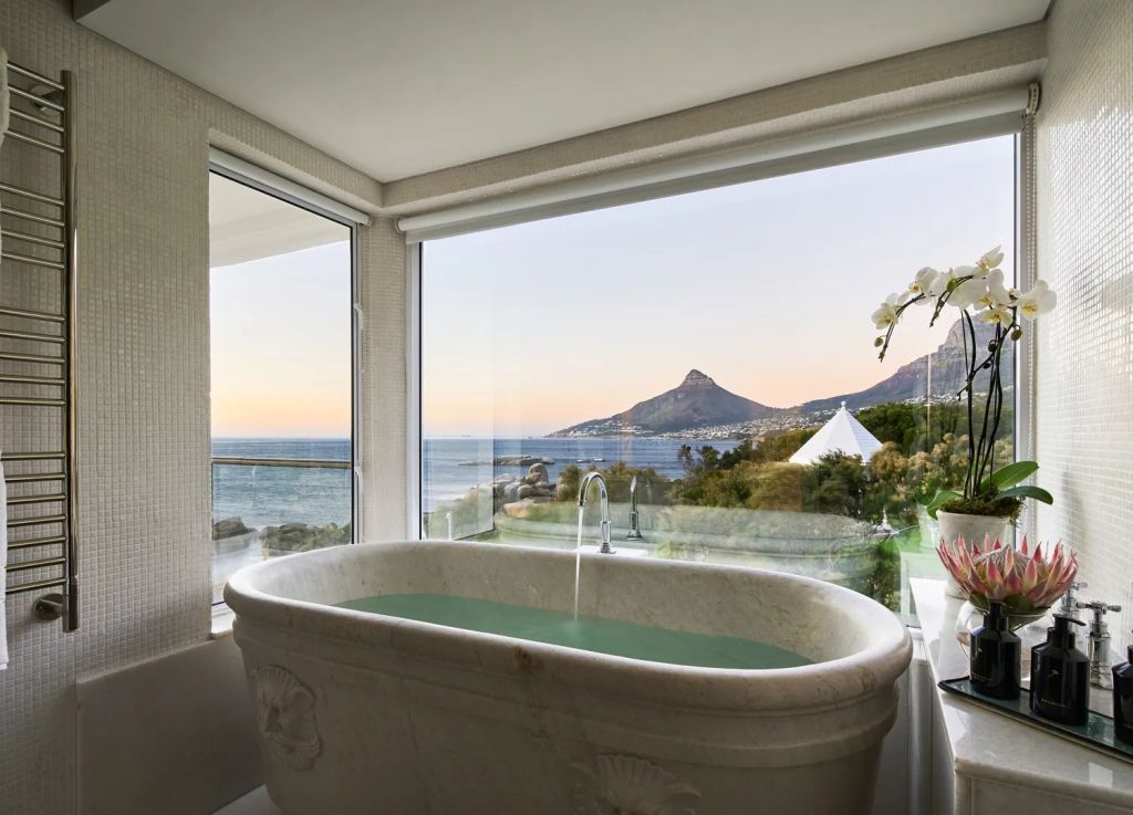 Freistehende Badewanne mit Panoramablick auf Meer und Berge bei Sonnenuntergang