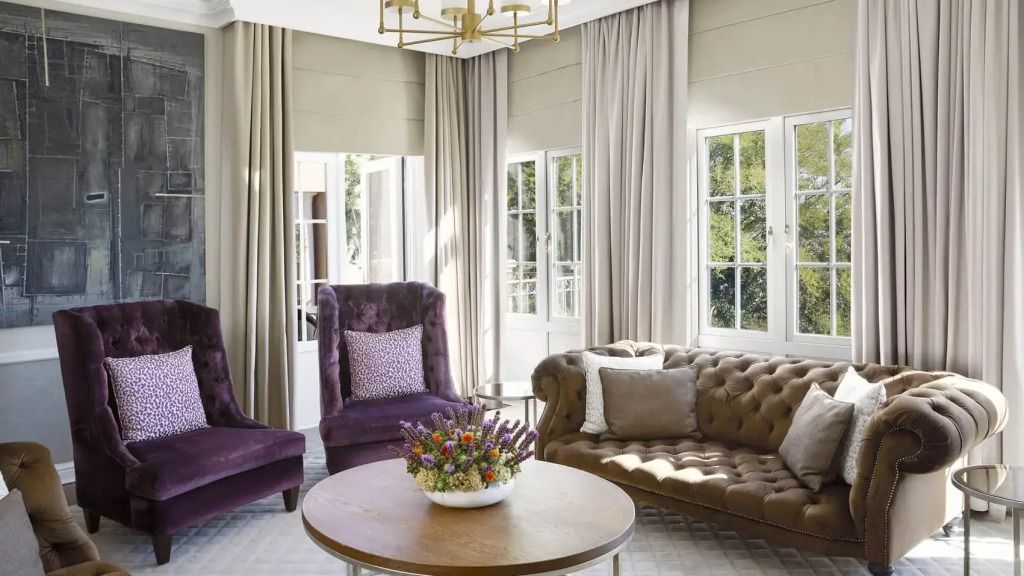 Elegantes Wohnzimmer mit violetten Sesseln, Sofa und großem Fenster mit Vorhängen.