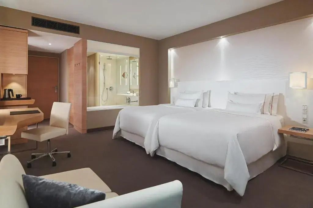 Geräumiges Hotelzimmer mit zwei Einzelbetten und modernem Badezimmer im Hintergrund.