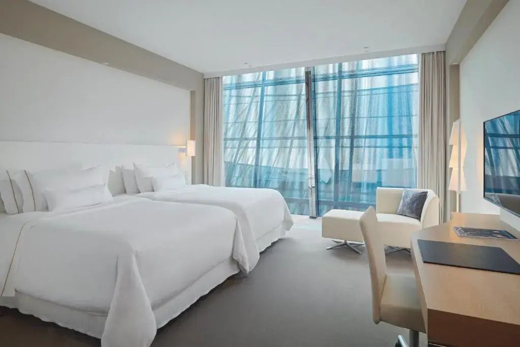 Hotelzimmer mit zwei Betten und großen Fenstern. Blick auf moderne Architektur.