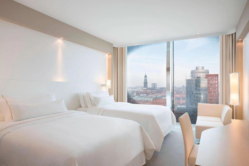 Modernes Hotelzimmer mit zwei weißen Doppelbetten und Blick auf die Hamburger Skyline