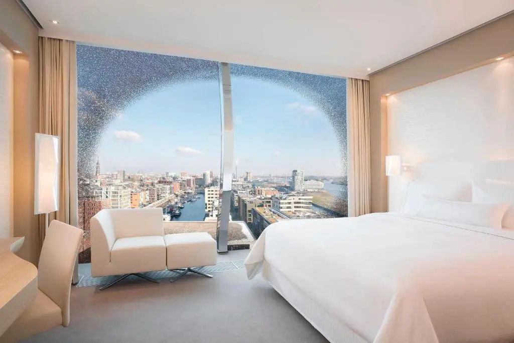 Hotelzimmer mit großem Doppelbett und weitem Blick über die Stadtlandschaft