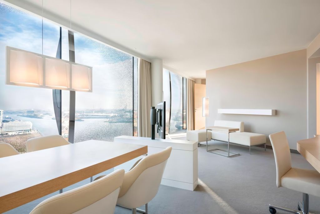 Helles Wohnzimmer einer Suite mit großem Fenster und Blick auf den Hafen