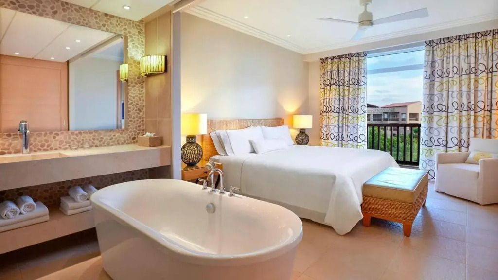 Modernes Zimmer mit freistehender Badewanne und Doppelbett neben großen Fenstern.