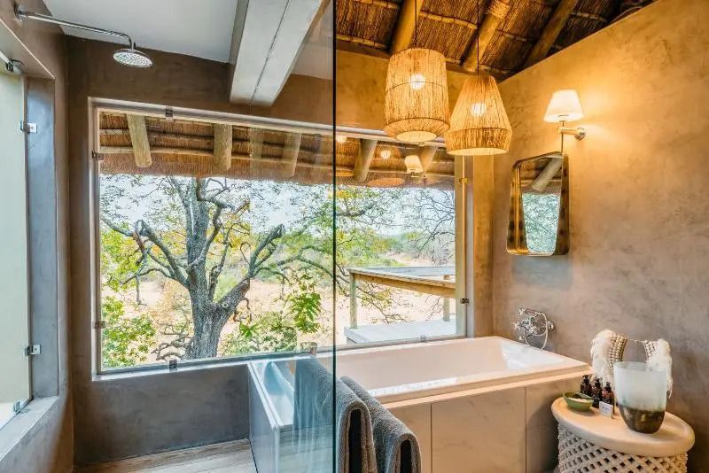Luxuriöses Badezimmer mit Badewanne und großer Glasfront mit Blick ins Grüne
