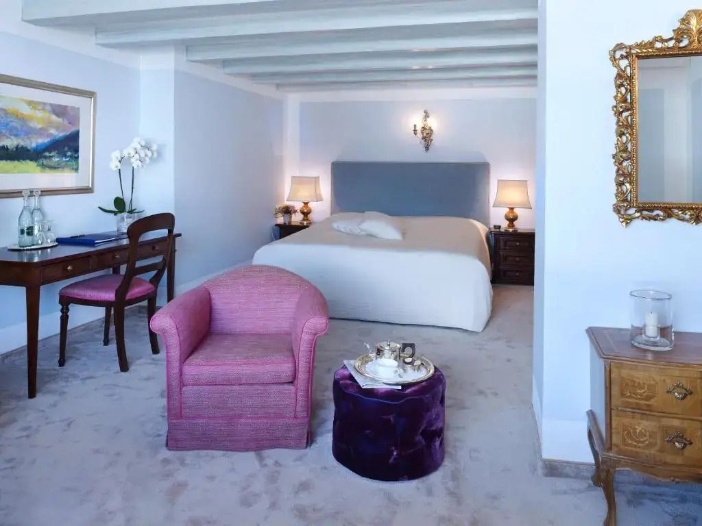 Helles Einzelzimmer mit einem großen Bett, rosa Sessel und Schreibtisch.