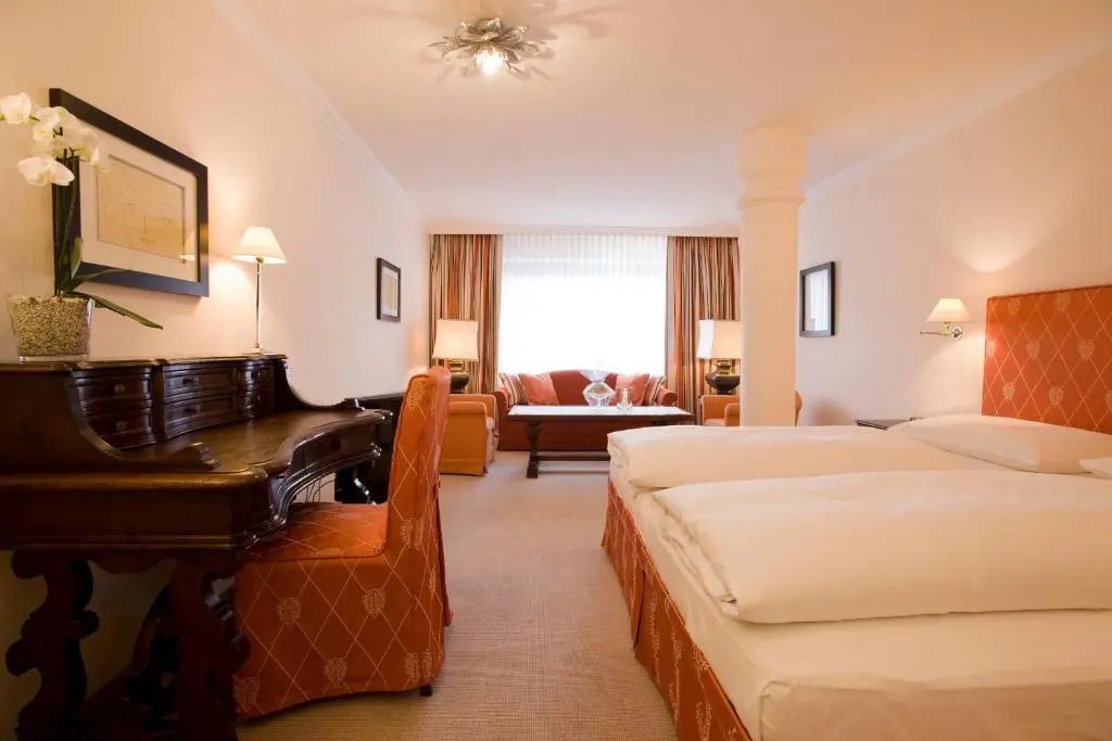 Geräumiges Einzelzimmer mit Doppelbett und Schreibtisch neben einem Sofa.