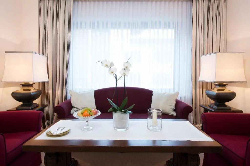 Sitzbereich mit rotem Sofa, Orchideen und Früchteteller auf Tisch.